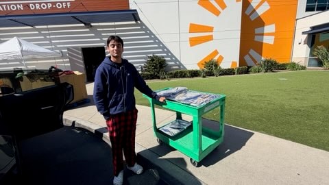 Volunteer with a green cart of meal trays at a donation drop-off