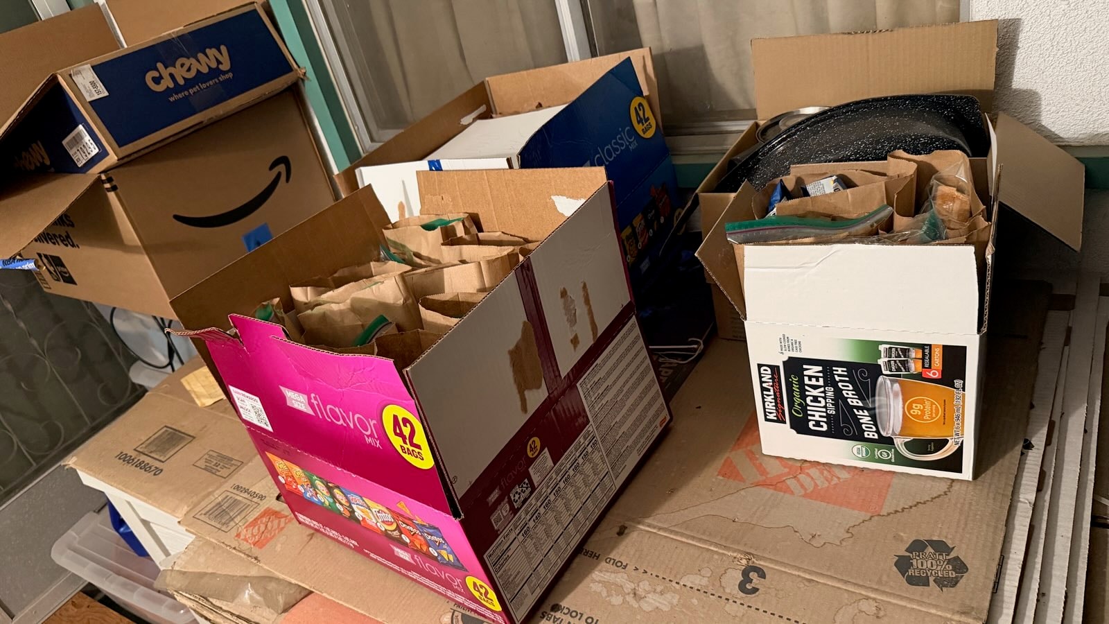 Boxes of Kirkland chicken bone broth, Chewy, and Amazon donations with meal bags